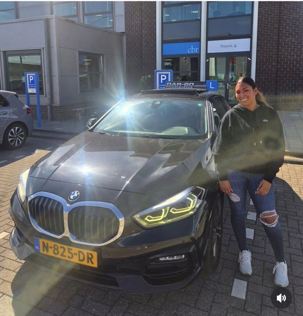 Geslaagde leerling bij DAR-GO rijschool poseert trots naast lesauto met L-bord na het behalen van rijbewijs