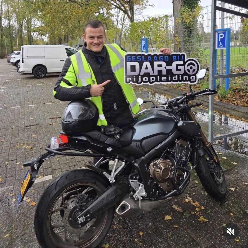 Geslaagde motorrijleerling van DAR-GO Rijopleiding poseert trots op motor na behaald rijbewijs