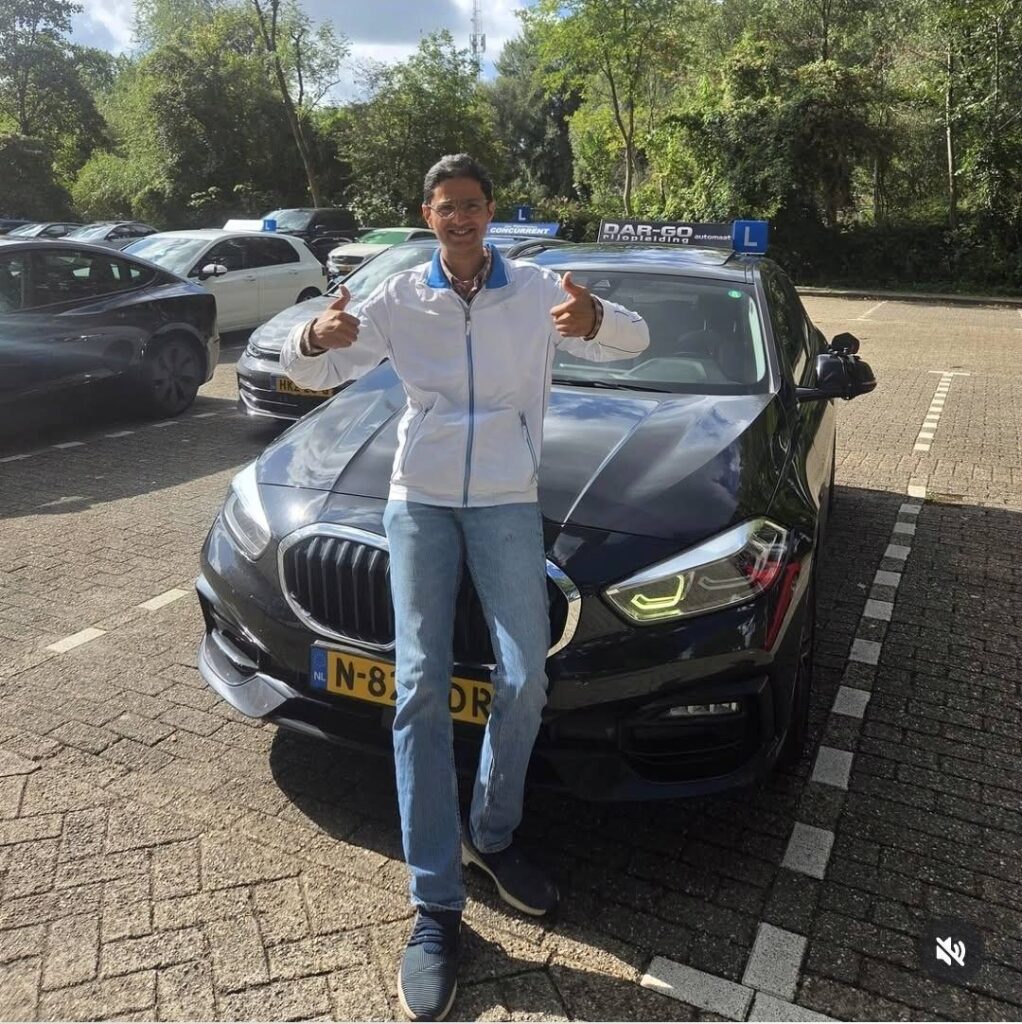 Geslaagde student van DAR-GO rijschool poseert trots met duimen omhoog naast BMW rijscholauto Geslaagde student van DAR-GO rijschool poseert trots met duimen omhoog naast BMW rijscholauto